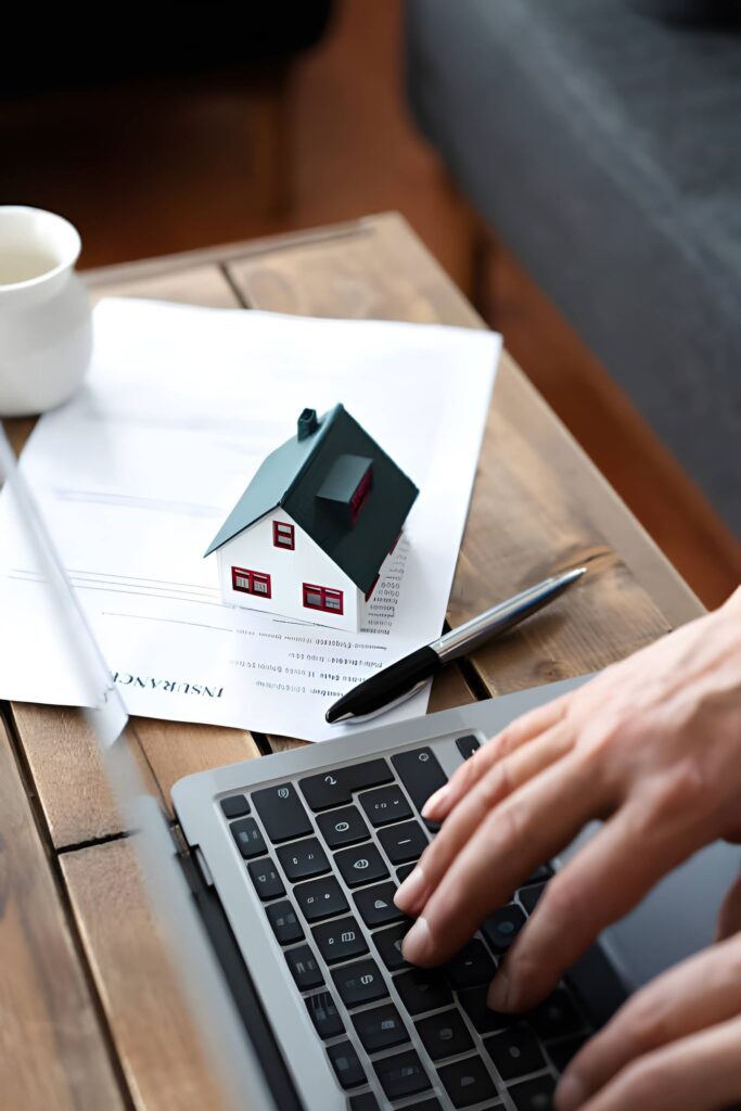 A person engaged in typing on a laptop, with a decorative house model on the table in front of them.